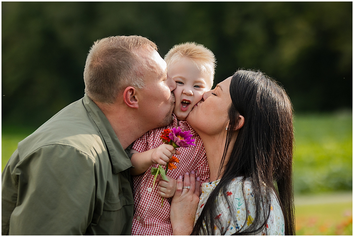 Parents kissing their son’s cheeks while he holds a colorful bouquet.