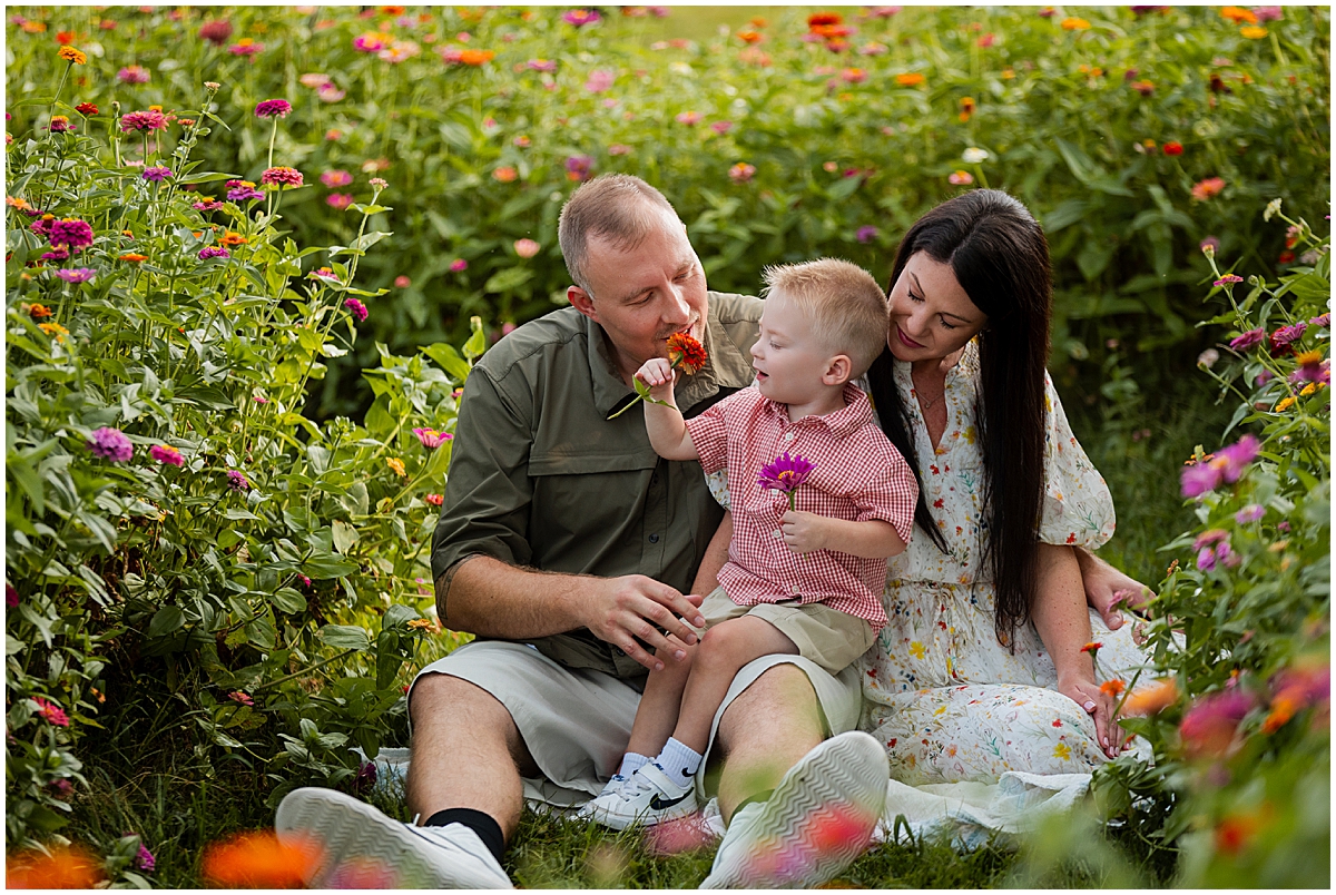 Young boy holding flowers while sitting with his parents among colorful blooms.