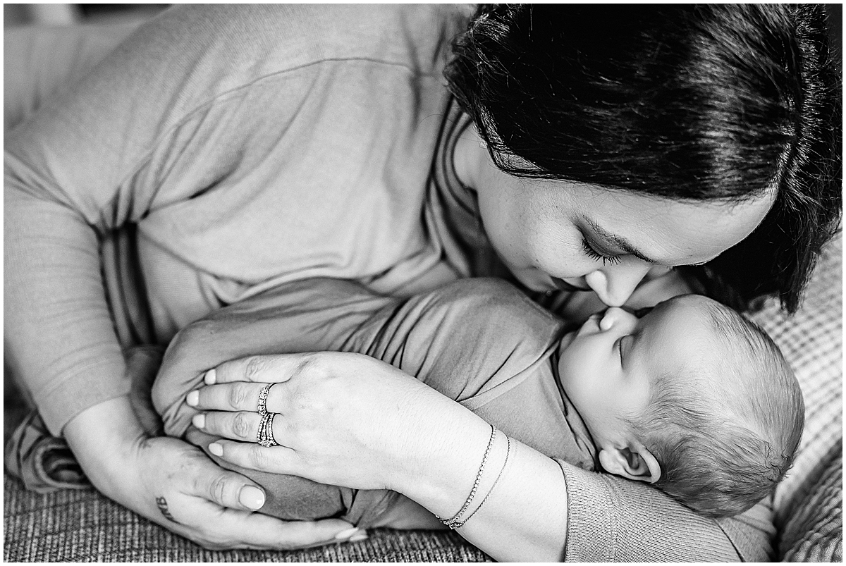 Black-and-white close-up of a mother kissing her swaddled newborn