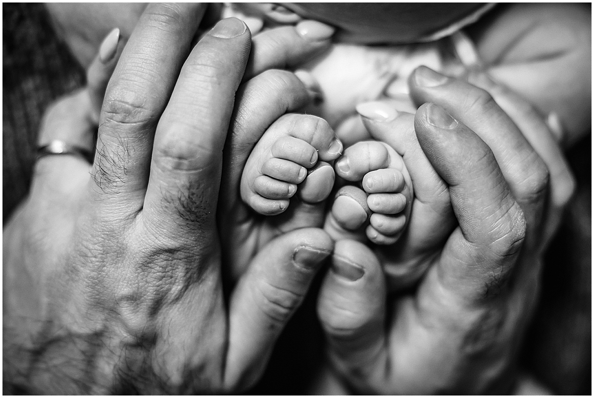 Black-and-white close-up of newborn feet cradled in parents’ hands
