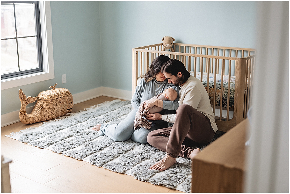 Family holding their newborn in a light blue nursery with wood furniture and a textured rug