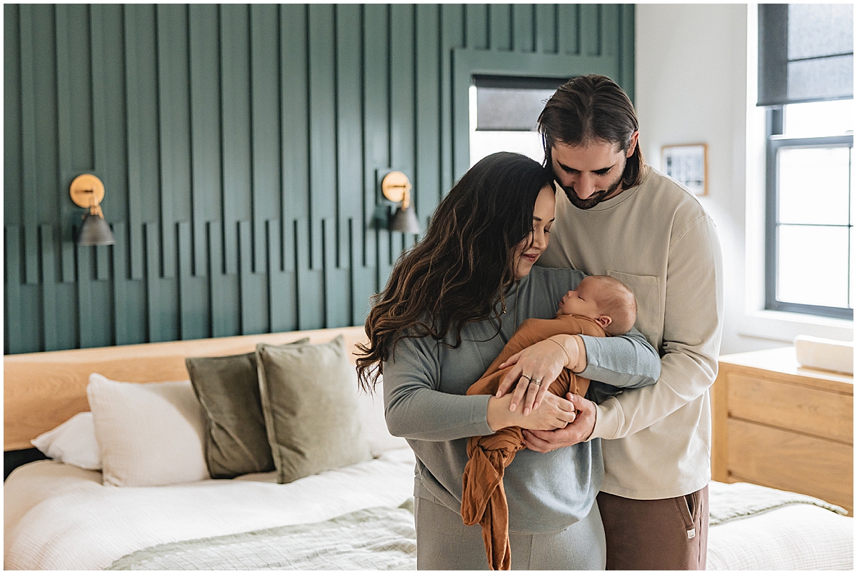 Mother in soft blue and father in cream standing together with their newborn in a brown wrap